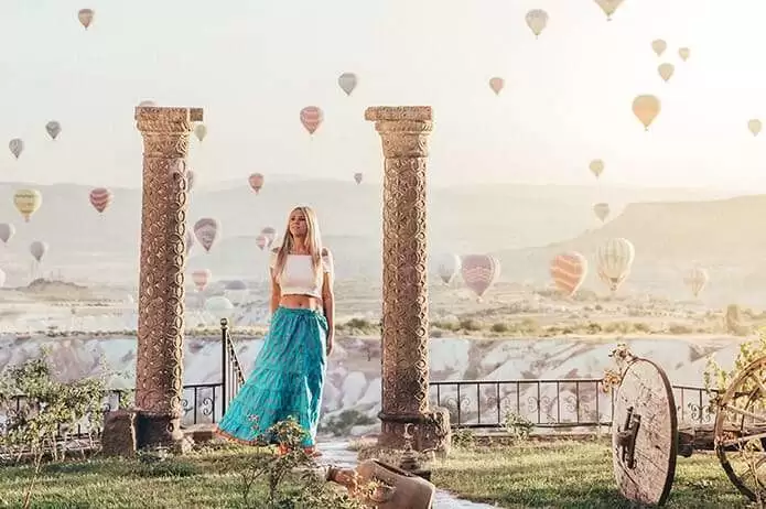 Museum Hotel web sitesi projesini anlatan liste görseli, fotoğrafta şapkası beyaz elbise giyen bir kadın, Museum Hotel havuzu önünde durup, sıcak hava balonlarını izlemektedir.