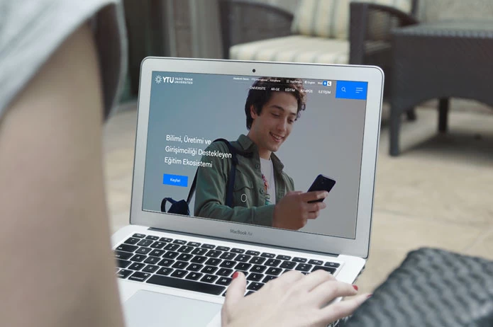 Yıldız Teknik Üniversitesi web sitesi projesini anlatan liste görseli, fotoğrafta elinde telefon olan genç bir kişi vardır